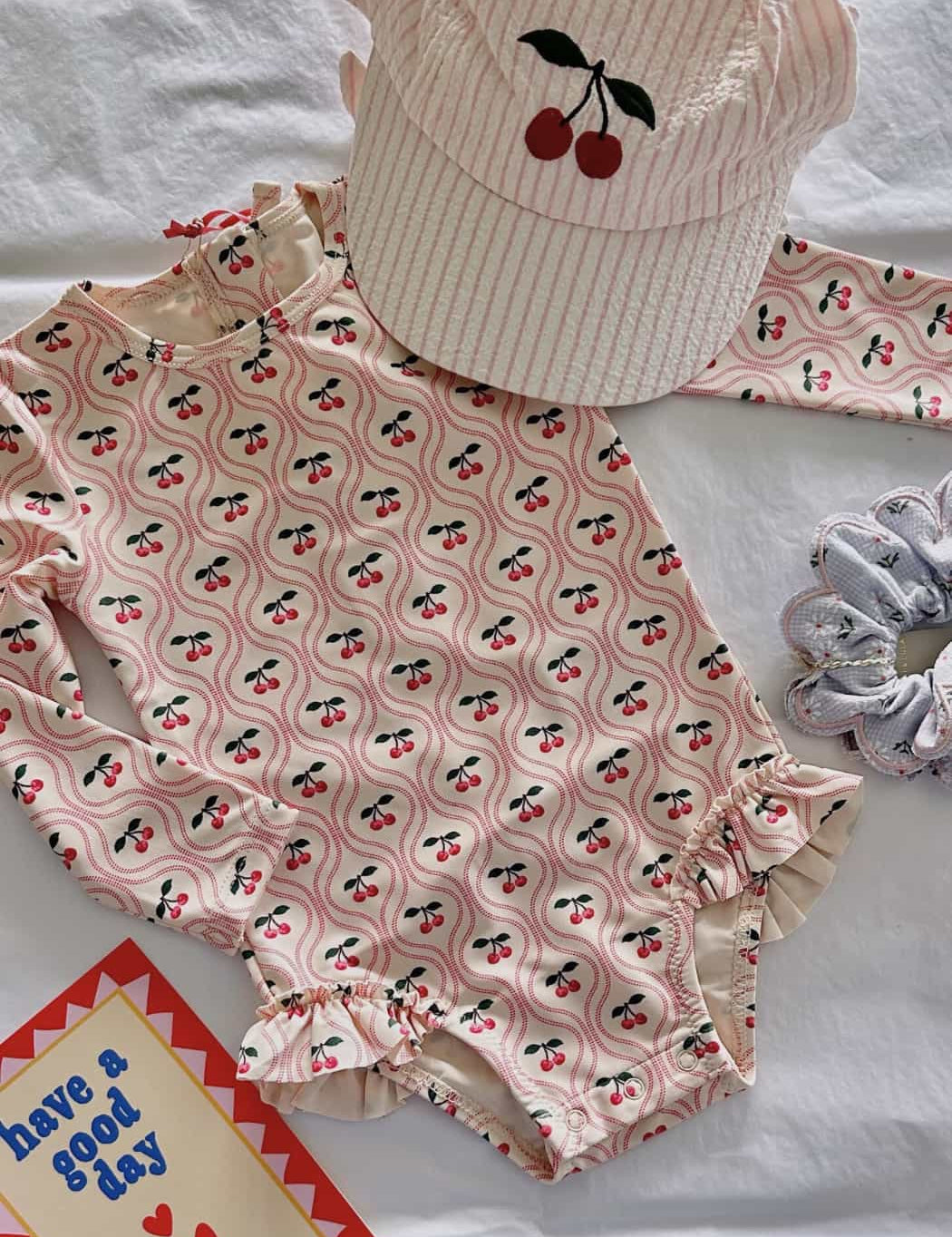 Children's swimsuit with cherry pattern and matching hat on a white background