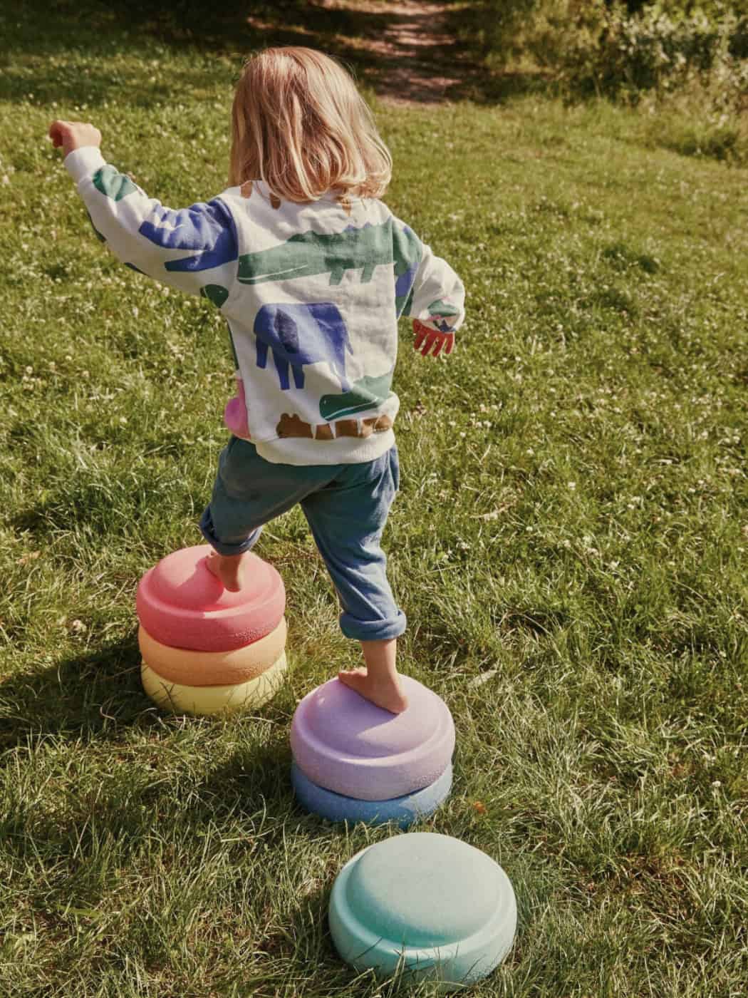 Child playing with colorful stepping stones on a grassy area