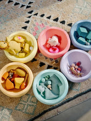 Set of colorful stapelstein stones being used upside down as bowls with toys on a patterned rug