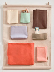 Fabric pockets in various colours hanging on a beige wall organiser.